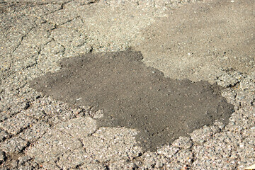 Cracked and patched asphalt on the road during a sunny day