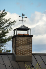 A brick chimney on a metal roof with a weathervane