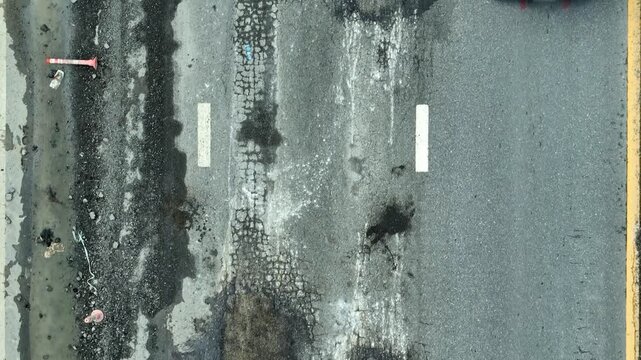 The worn and crumbling asphalt road illustrates gaps in city planning, maintenance delays, safety risks, resource shortages, increased environmental harm, and the need for resilient infrastructure.
