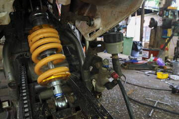 Close up view of yellow motorcycle shock absorber and suspension during repair in workshop. Focus on mechanical parts, brake system, and chain during vehicle maintenance