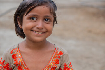 Smiling little girl in colorful traditional dress standing outdoors in a rural village setting