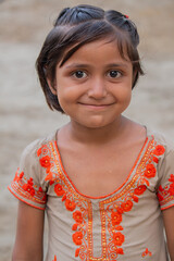 Smiling little girl in colorful traditional dress standing outdoors in a rural village setting