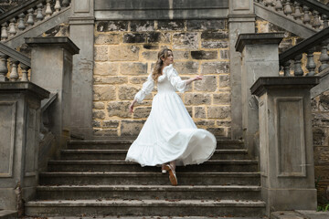 Naklejka premium Full length female figure of blonde model wearing white fantasy wedding gown. Back view pose, walking away on historical staircase of castle location 