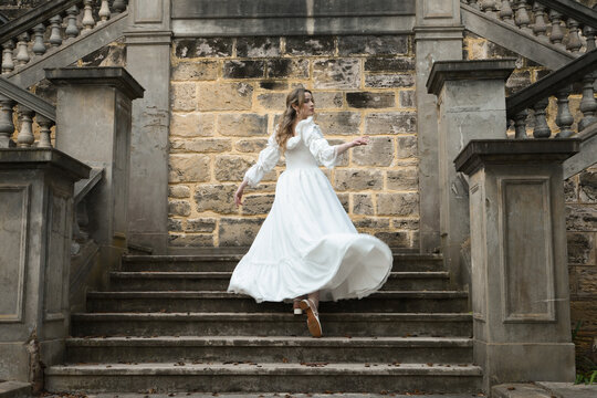 Full length female figure of blonde model wearing white fantasy wedding gown. Back view pose, walking away on historical staircase of castle location 
