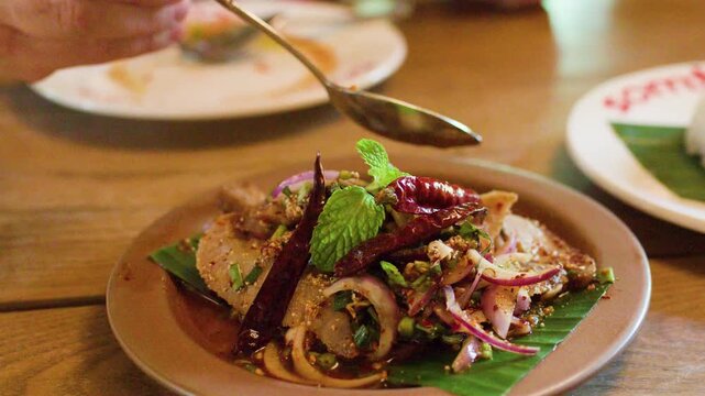 Garnishing Spicy Thai Pork Salad with Fresh Herbs and Chili