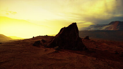 Vibrant golden hues fill the sky as the sun sets behind distant mountains. A prominent rock stands silhouetted against the colorful backdrop, highlighting the beauty of the landscape.