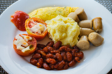 Healthy breakfast menu of mashed potatoes, omelet, read beans, tomatoes, and sausages served on a white plate