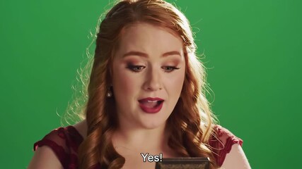 A young excited woman with long red hair and a vibrant red top reacts with surprise and joy exclaiming Yes while holding a small ornate object against a bright green screen background perfect for chr.