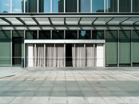 Modern glass building entrance with canopy, reflections, and urban path
