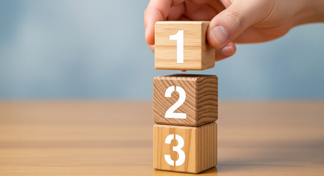 Hand stacking wooden blocks with numbers one two and three representing steps or priorities on a wooden surface