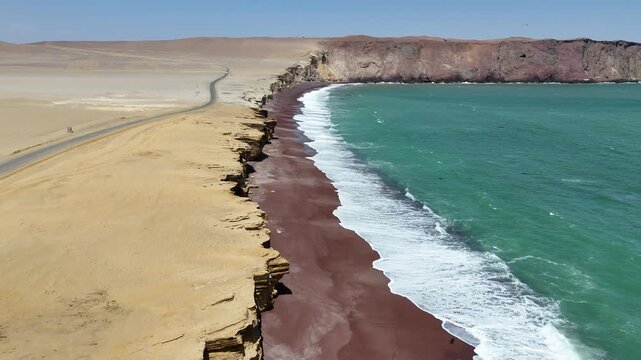 Numerous waves crashing forcefully onto the iconic red sand Playa Roja beach in Peru's Paracas National Reserve, highlighting the dramatic coastal contrast