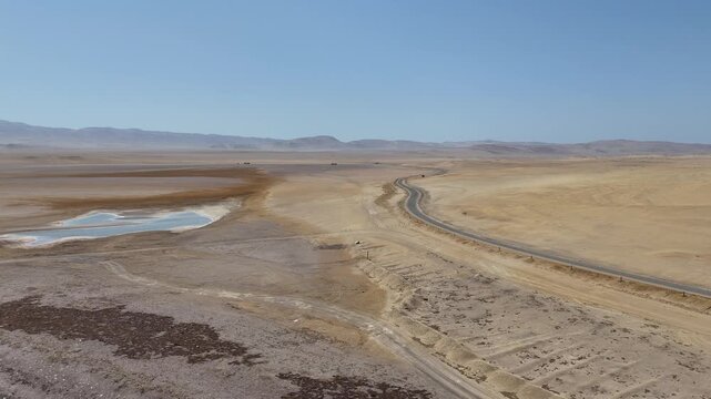 Moving forward captures an aerial view of a paved road running along the arid desert coastline of the Paracas National Reserve in Peru, a UNESCO World Heritage site where the desert meets the Pacific 