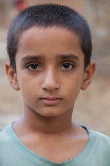 Close-up portrait of a young Pakistani boy with short hair wearing light blue shirt and serious expression