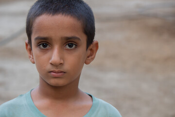 Close-up portrait of a young Pakistani boy with short hair wearing light blue shirt and serious expression