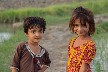 Two smiling rural children standing near a field path in warm evening light, showing innocence and friendship