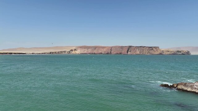 Moving forward across the turquoise waters of Paracas Bay toward the large, arid, red-hued desert cliffs on the far side of the Paracas National Reserve