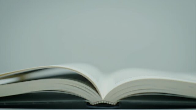 An Open Book With White Pages Flipping Gently in Soft Ambient Light on a Light Gray Background