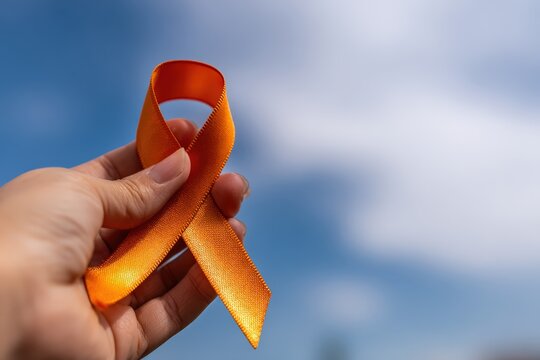 Hand holding an orange awareness ribbon, symbolizing support and hope for conditions like MS, leukemia, ADHD, and kidney cancer