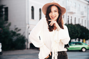 Obraz premium Portrait of young beautiful smiling hipster woman in trendy summer white blouse and jeans. Carefree woman posing in the street in sunny day. Positive model outdoors. Cheerful and happy