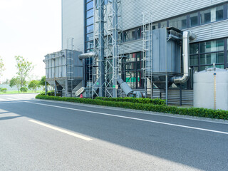Industrial building with water tank, pipes, and greenery by road