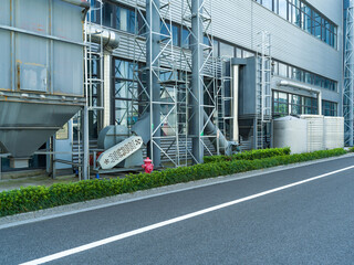 Industrial building with water tank, pipes, and greenery by road