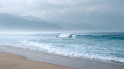 Serene ocean waves crash on a sandy beach with distant misty mountains under a soft atmospheric sky