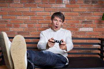 A middle-aged man gamer holds a gamepad and plays an online game on a computer.