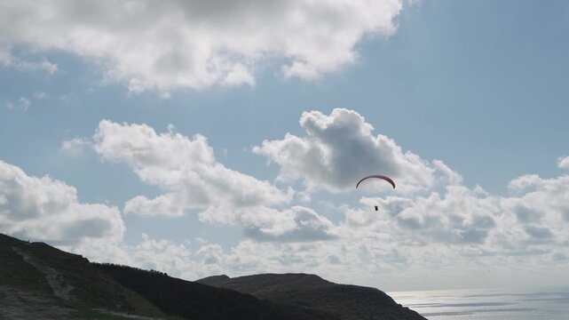 Flight of a red paraglider against the background of blue sky, clouds and mountains