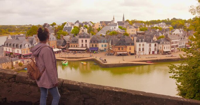 A woman enjoys the picturesque view of Saint-Goustan port in Auray, France. The scene captures charming architecture and tranquil waters, evoking a peaceful, reflective mood.