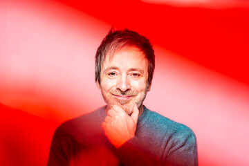 Mid 50s Man Smiles Engagingly in Front of a Warm, Colorful Background