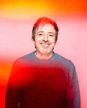 Man in His Mid 50s Smiles Warmly Against a Colorful Background in a Cheerful Setting