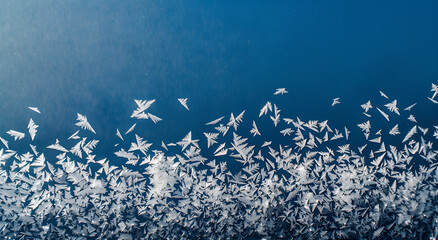 Zamarznięte wzory lodu na szybie z niebieskim tłem – naturalna tekstura mrozu w geometrycznych kształtach.