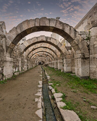Ancient Roman arches and a water channel at the Agora of Smyrna, Izmir, Turkey, under a cloudy sky