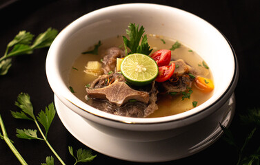 Warm Oxtail Soup Sop Buntut on a white ceramic bowl Indonesian Restaurand Food with Spices, Carrot, Lime, Corriander Leaves