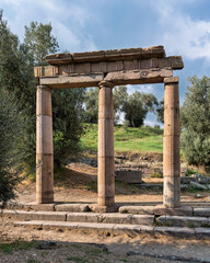 Asclepieion of Pergamon, Bergama, Turkey. Ancient ruins featuring three stone columns and a lintel, surrounded by olive trees and green hills under a blue sky.
