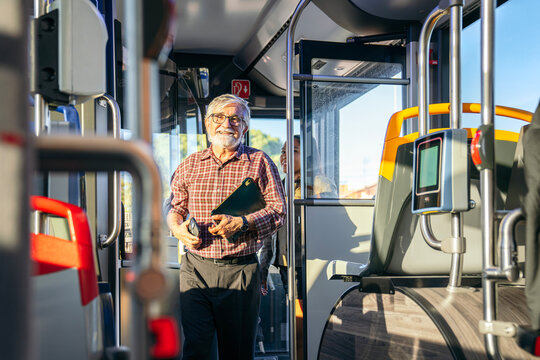 Senior man smiling, walking in a public transport bus. Commuting in the city using urban transportation