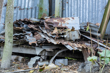Weathered and deeply rusted corrugated metal scraps, bent and broken, are stacked in a disorganized...