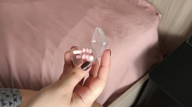 A container with pink earplugs in the girl's hands. Sleeping in silence