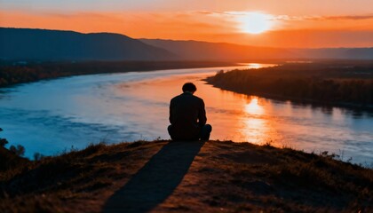 Man sitting on edge of mountain at sunset looking at river thinking about life enjoying view