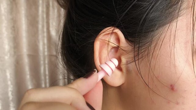 Brunette girl wearing pink earplugs. A woman inserts earplugs. Sleeping in silence