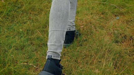 Traveler wearing black shoe stepping through forest grass revealing habitat imbalance and biodiversity loss. Explorer moving toward fallen tree showing deforestation impact and conservation need