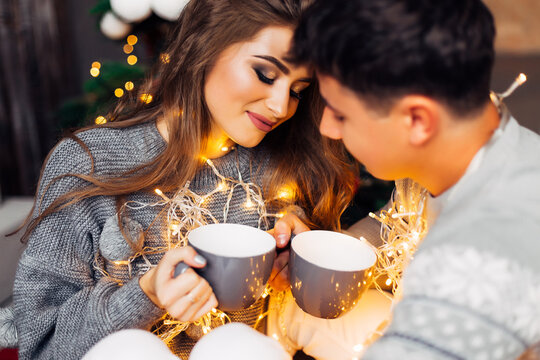 couple in love wrapped in garlands sitting and holding cups. bea