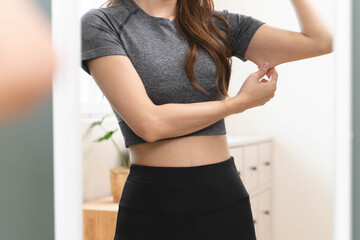 Body care and weight loose concept, Close-up shot of woman looking at mirror grab her skin around under arm and worry about her figure. © Pormezz