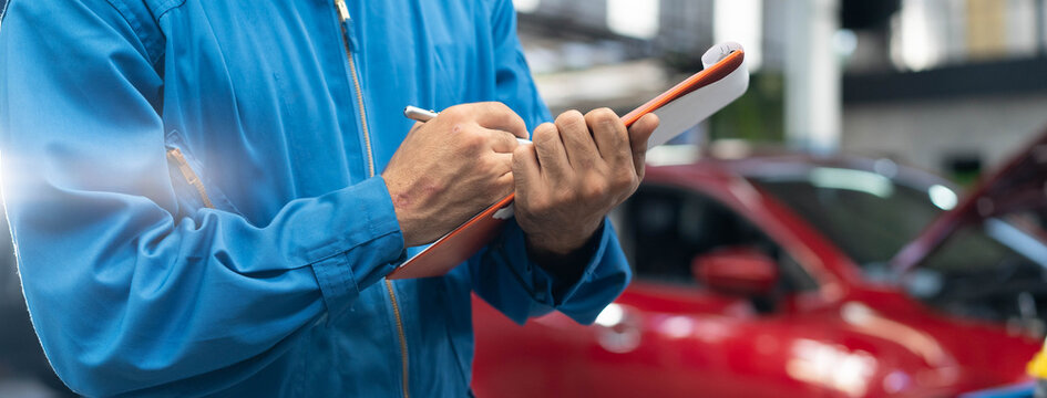 Auto check up and car service shop concept. Mechanic writing job checklist to clipboard to estimate repair quotation to client at workshop garage.
