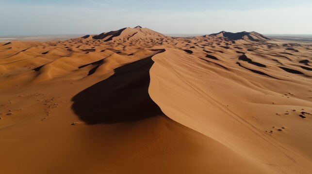 An aerial view of a vast desert landscape featuring tall sand dunes, casting shadows under a clear sky
