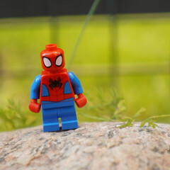 Naklejka premium lego spiderman figure standing on a rock with a blurred green background