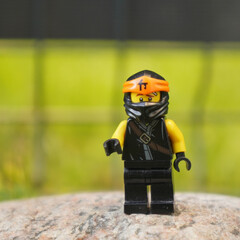Naklejka premium Lego Ninjago Jay minifigure standing on a rock with a blurred green background