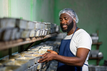 African male baker, successful small business owner inspecting risen bread dough balls in metal...