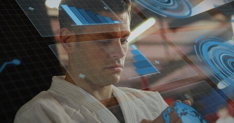Interacting man wearing white gi at control room, moving holographic globe with floating charts