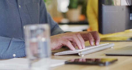 Typing man in blue shirt using white wireless keyboard at office desk, with smartphone and papers